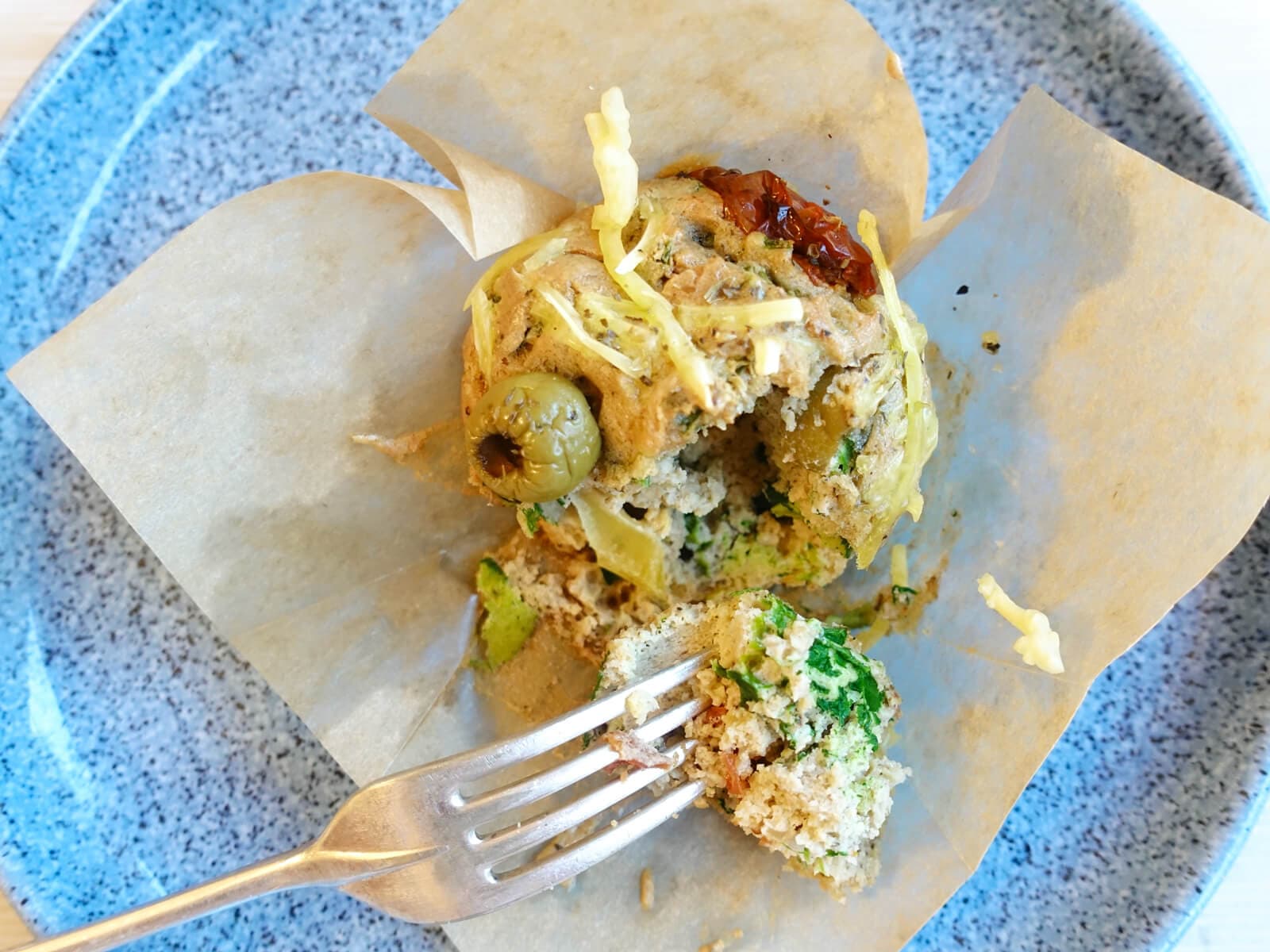 A muffin made with spinach and tomatoes, individually wrapped, shown here on a plate with a fork. Another delicious mental health recipe from the Inflammation Pioneer.