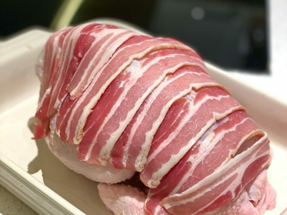 Chicken wrapped in bacon, in a roasting tin, ready to go in the oven.