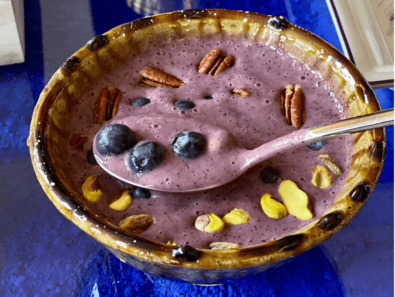 A bowl of banana and blueberry smoothie with nuts and blueberries on top.