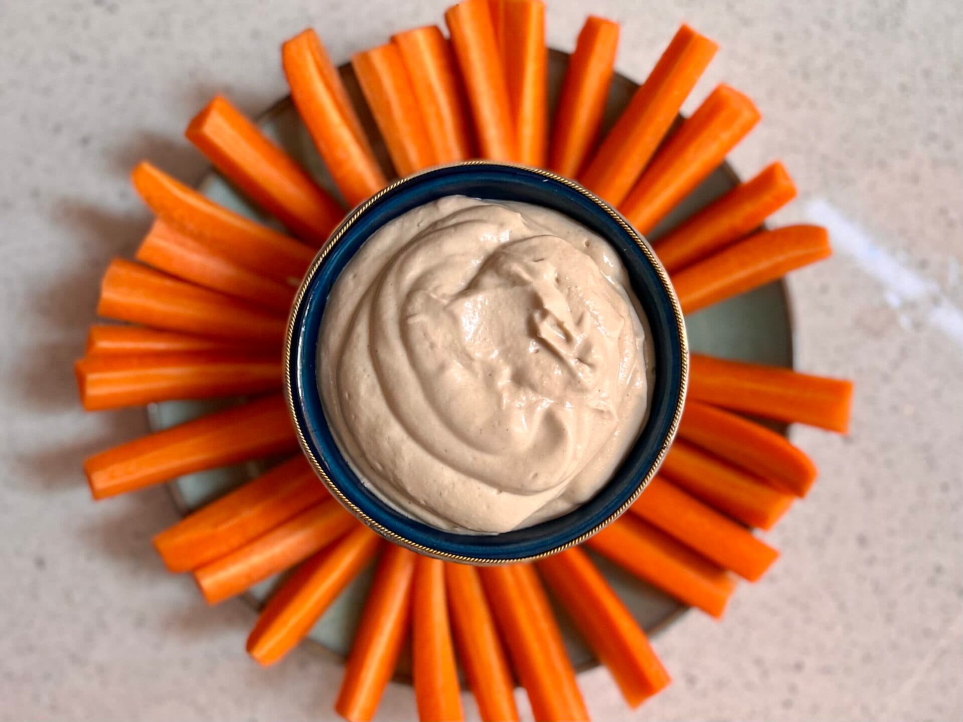 A plate of carrot sticks with a pot of tahini dip in the middle.