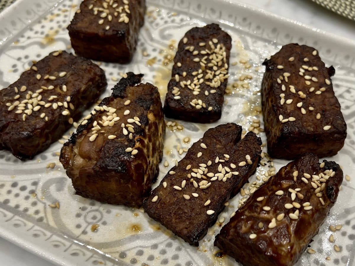 Slices of teriyaki tempeh that have been marinaded, baked, and topped with sesame seeds.
