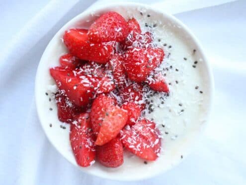 A bowl of coconut yogurt with strawberries and chia seeds on top.