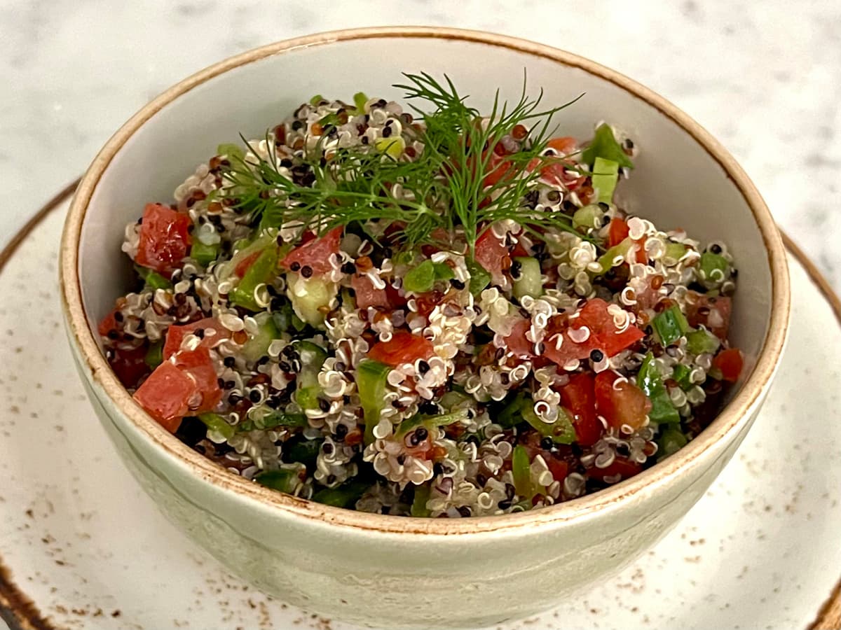 A close-up of a bowl of quinoa with tomatoes and cucumber with herbs.