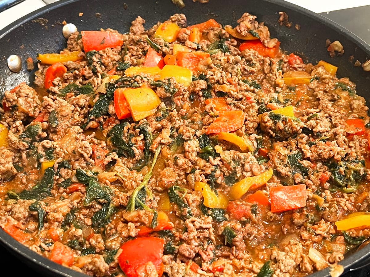 in a frying pan there is beef mince, red and orange bell peppers, wilted spinach and seasoning