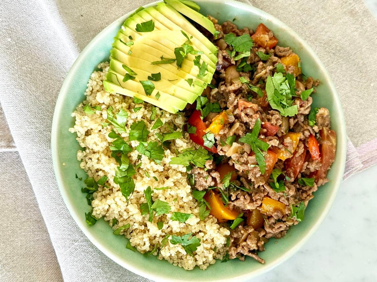 Mexican Ground Beef in a bowl with cooked quinoa and half and avocado garnished with chopped cilantro