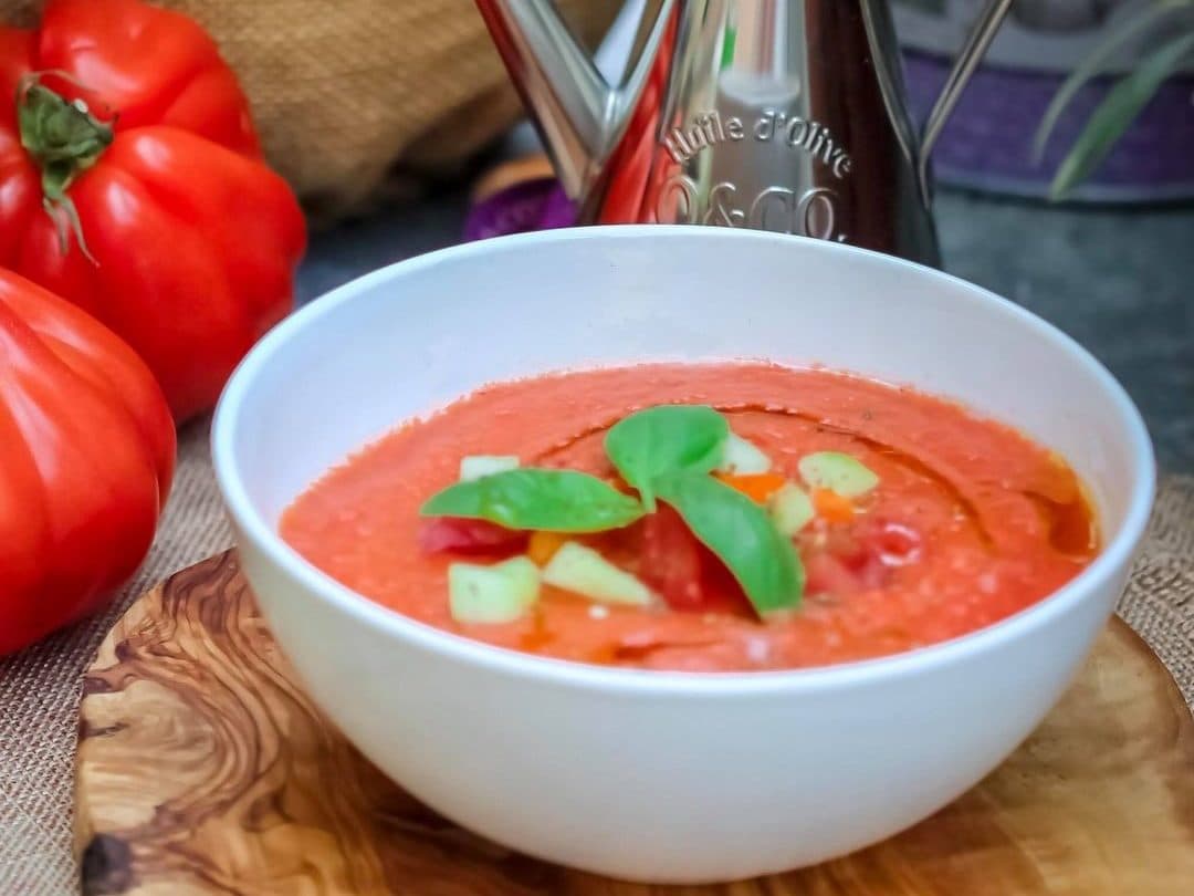 A bowl of bright red gazpacho, topped with cucumber, pepper and basil.